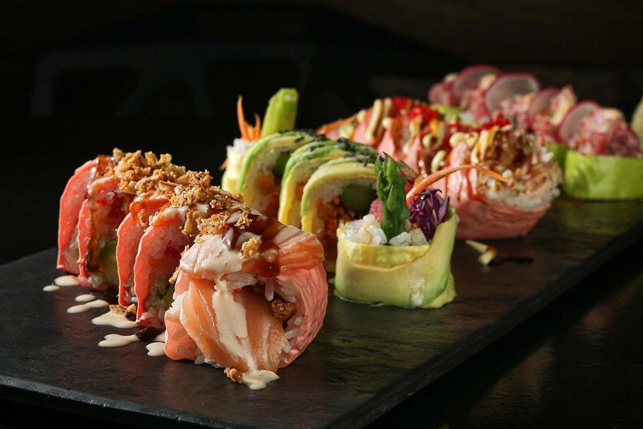 Specialty makis topped with salmon and avocado on black slate