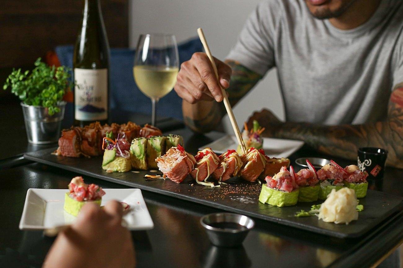 Chopsticks over a board of makis, white wine on the table