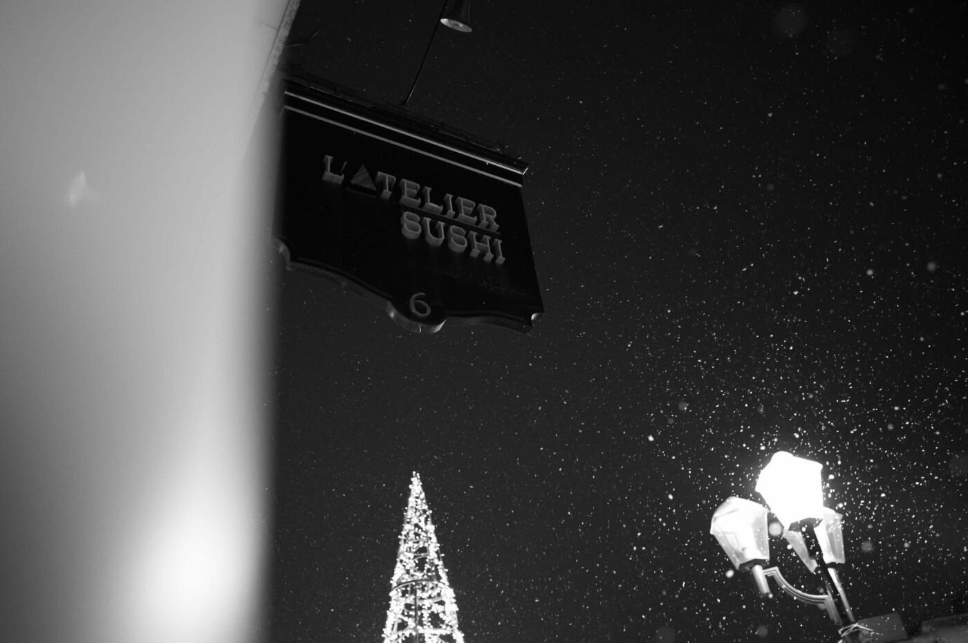 The hanging L’Atelier Sushi sign outside on a winter night